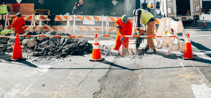 Construction workers repairing a road, surrounded by orange cones and barriers.