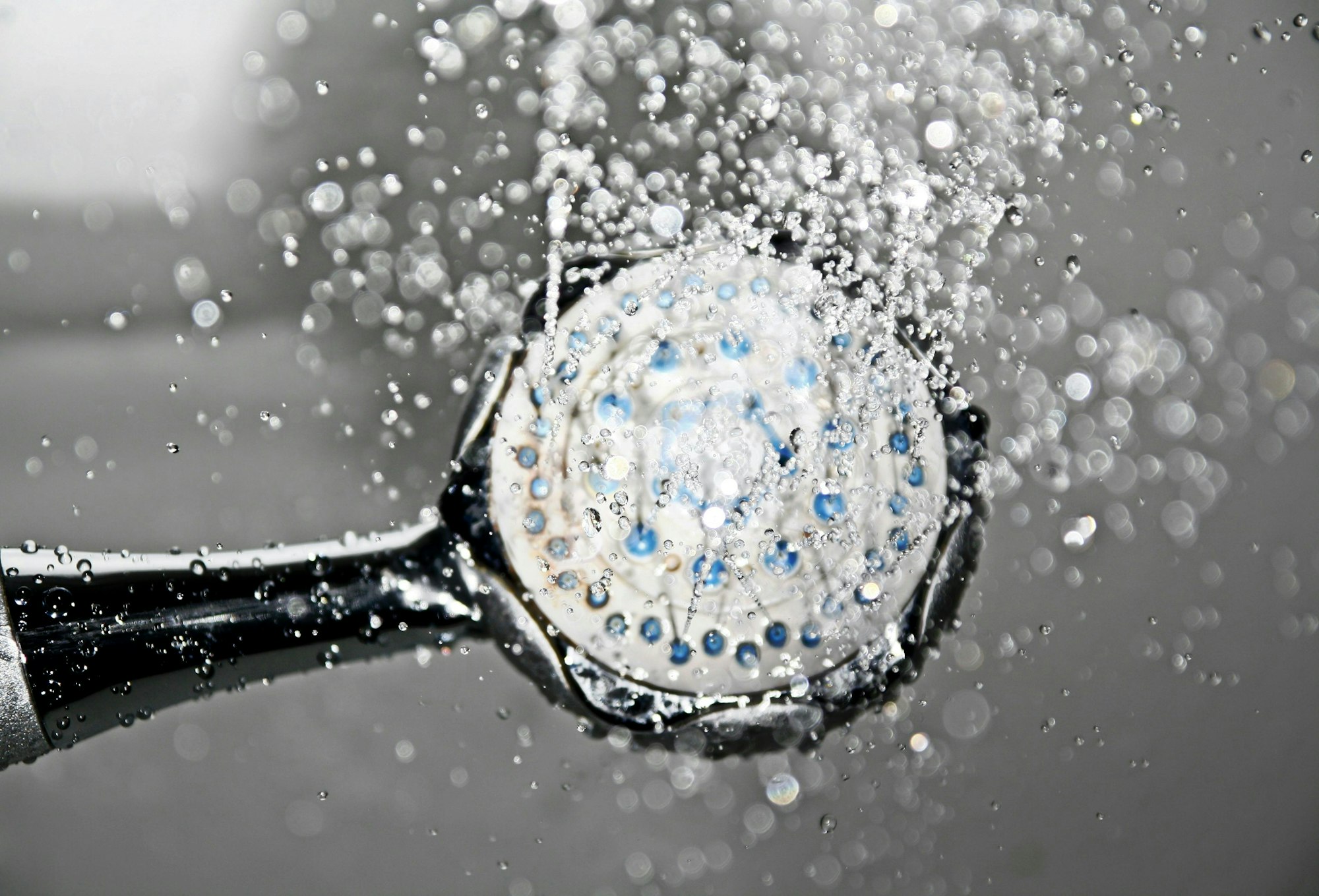 Showerhead with flowing water and droplets suspended in the air, captured in motion, against a blurred background.