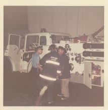 Three people near a white fire truck, one wearing a "Fire Dept" jacket.