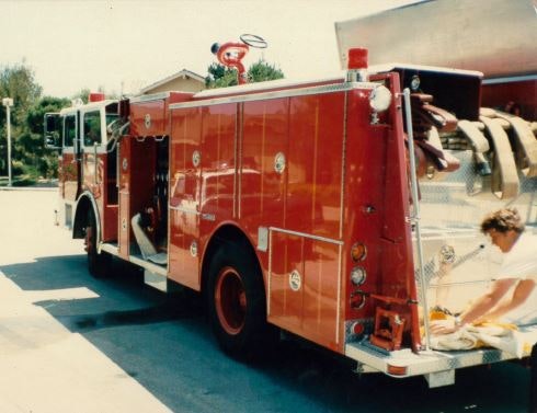 A red fire truck is parked, with hoses visible, and a person is working near it.