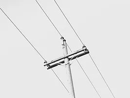 A black and white image of a utility pole with electrical wires against a plain sky.