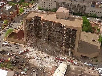 A large, partially collapsed building with debris and emergency vehicles surrounding it.
