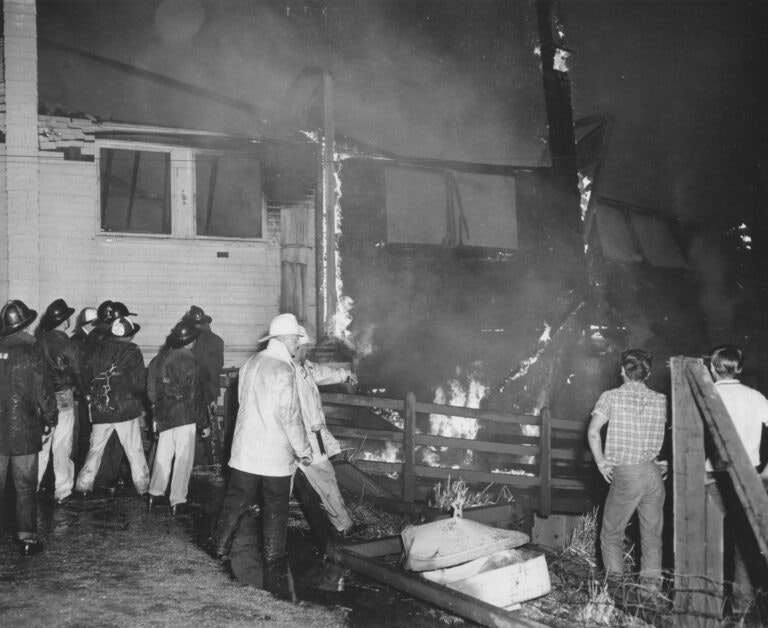 Firefighters extinguishing a building fire at night with flames visibly engulfing the structure.
