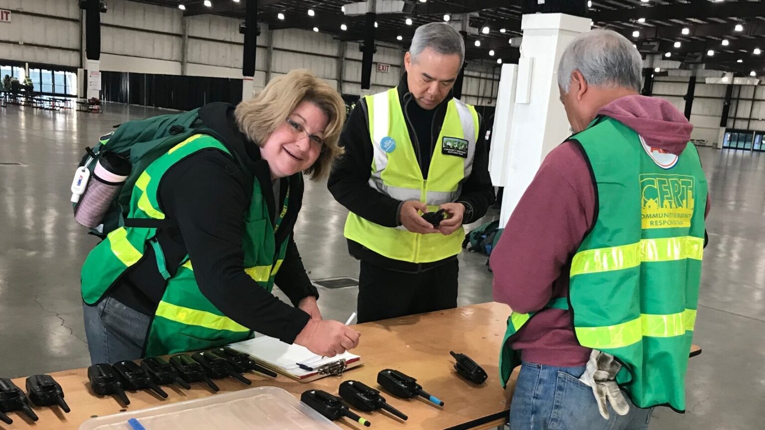 People in safety vests at a table with radios, involved in coordination or training, possibly for emergency response.