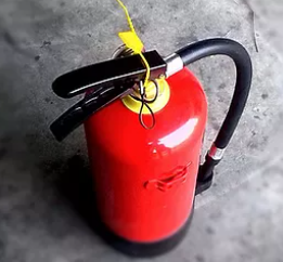 A red fire extinguisher with a black hose and a yellow safety seal on a gray surface.