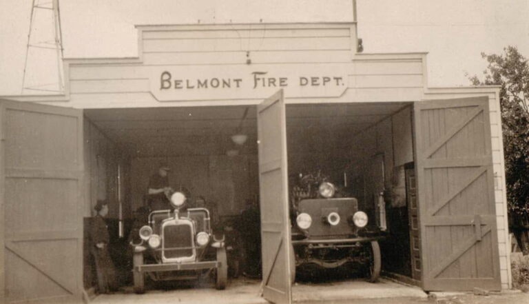 Old Belmont Fire Dept. station with two vintage fire trucks inside, doors open.