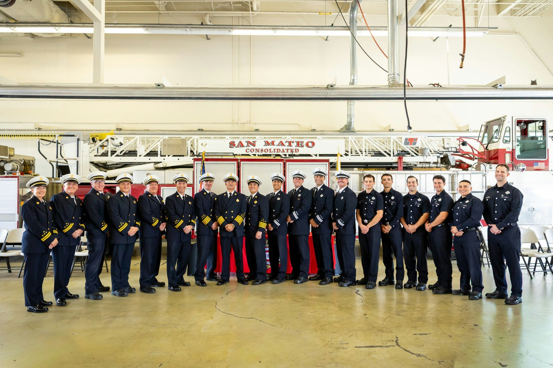 A group of firefighters in uniform posing in front of a fire truck at a station labeled "San Mateo Consolidated."