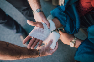 A person is getting their hand bandaged by another, wearing a watch and blue clothing.