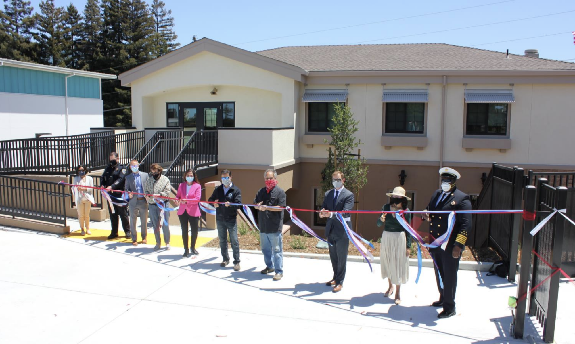 A group of people standing outdoors at a ribbon-cutting ceremony in front of a building.