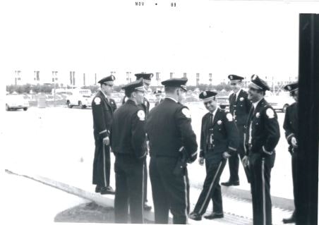 A group of uniformed officers are gathered outside, standing in a parking lot area.
