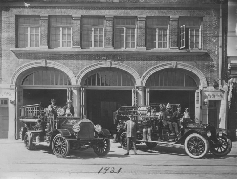Vintage fire engines and firefighters in front of a fire station, 1921.