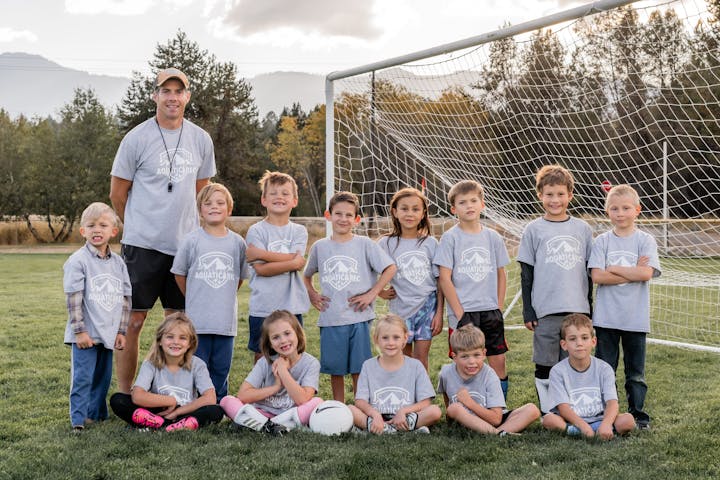 May contain: people, person, ball, football, soccer, soccer ball, sport, clothing, t-shirt, grass, plant, child, female, girl, boy, male, adult, man, footwear, shoe, pants, team, groupshot, accessories, jewelry, necklace, and hat