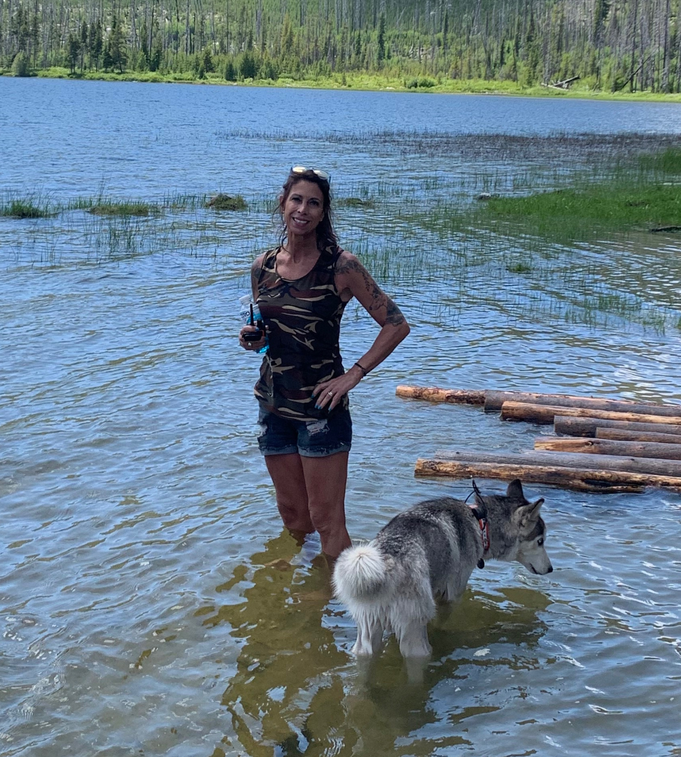 May contain: clothing, shorts, plant, vegetation, face, head, person, photography, portrait, water, waterfront, tree, lake, nature, outdoors, wood, adult, female, woman, animal, canine, dog, mammal, pet, and husky