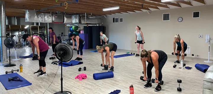 A group workout session with women using weights in a fitness studio, featuring mats and exercise equipment.