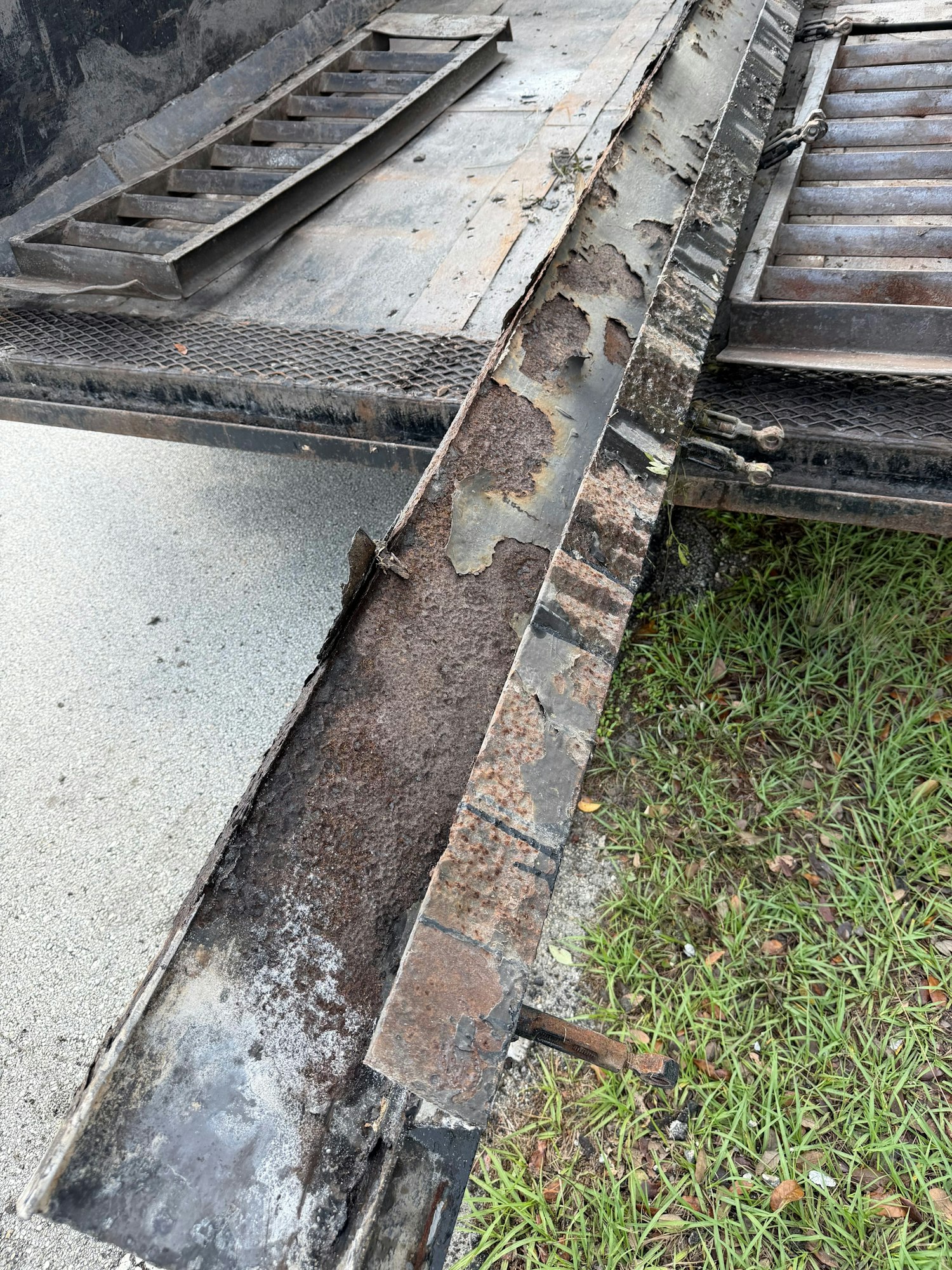 The image shows a close-up of a weathered metal surface with rust and peeling paint, alongside grass and concrete textures.