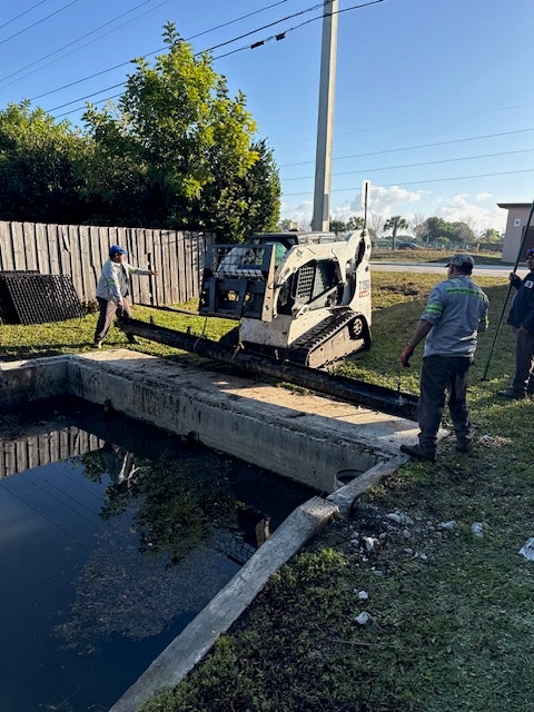 A vehicle near a drainage area with workers near water and vegetation, performing maintenance or repairs.