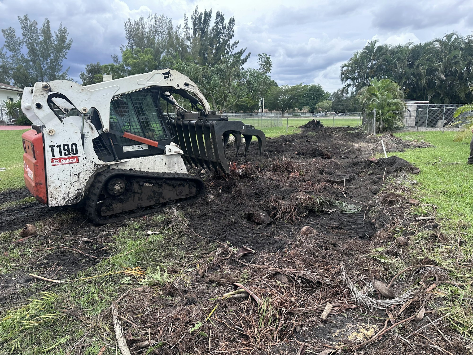 Skid steer loader clearing land, moving dirt and debris in an outdoor area.