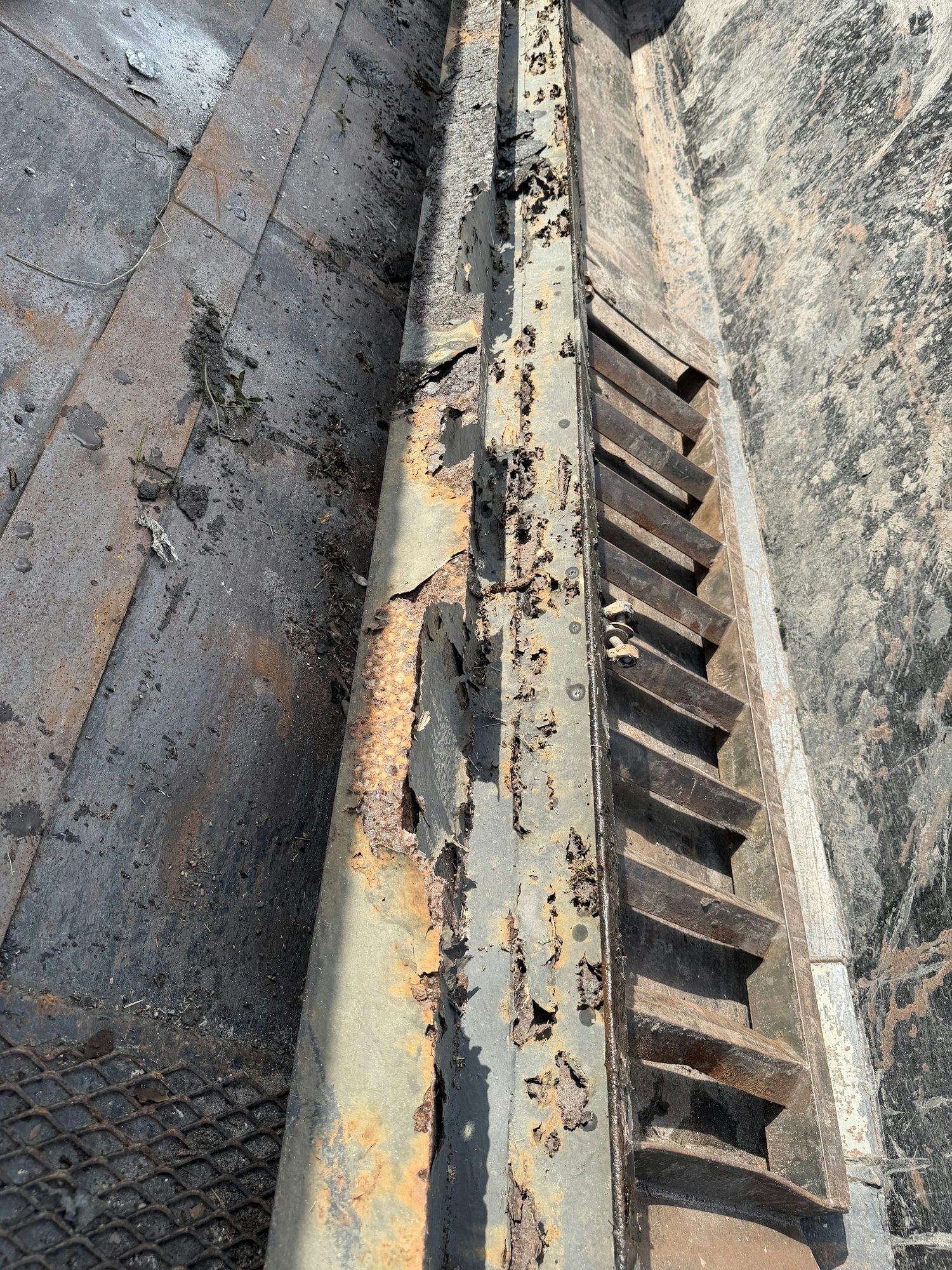 The image shows a rusted, corroded metal structure, likely part of a larger mechanism, with debris on a weathered surface.