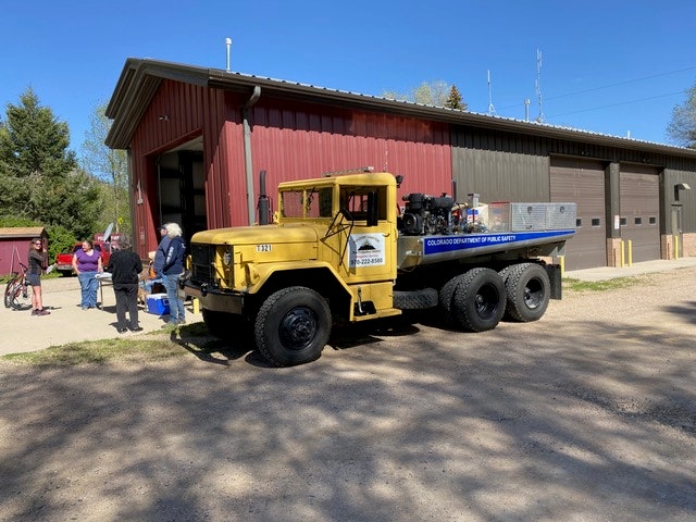 A yellow truck labeled "COLORADO DEPARTMENT OF PUBLIC HEALTH" parked outside a building, with people in the background.
