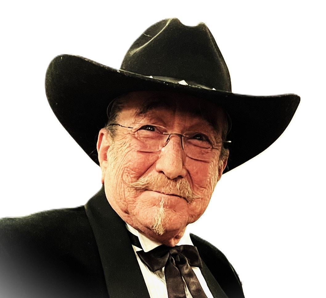An older man with glasses, wearing a black cowboy hat and suit with a bow tie, against a white background.