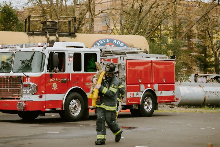 Firefighter in gear carrying equipment near a red fire truck labeled "Santa Rosa."