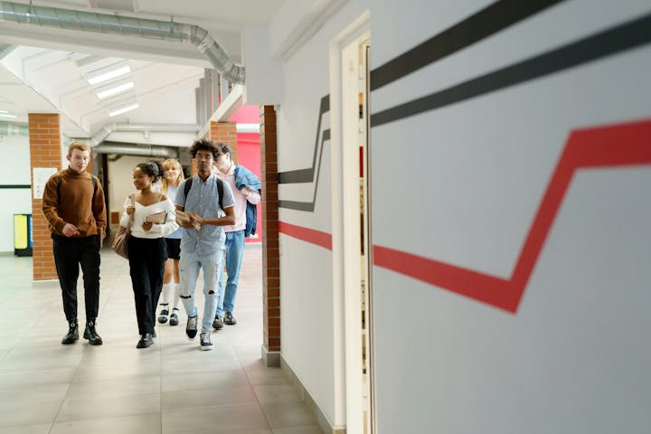 A group of young adults walking in a hallway, holding books and backpacks.