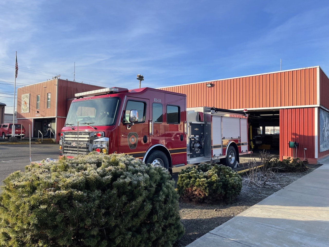 A red fire truck parked by a fire station with an open garage door, under a clear sky.
