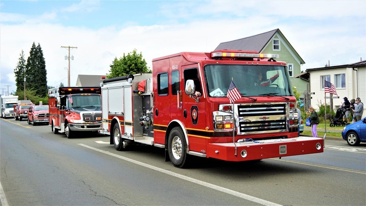 A red fire truck with American flags in a parade on a street.