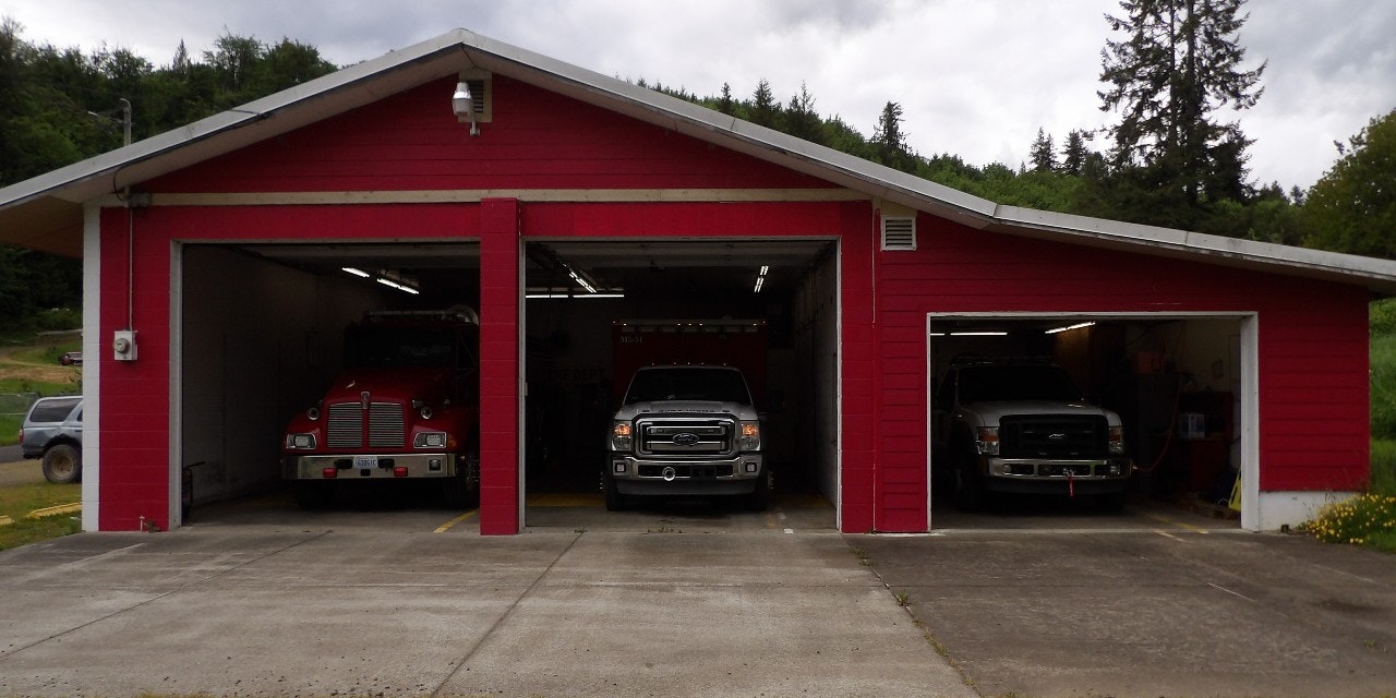 A red fire station with open bays revealing a fire engine and two trucks inside.