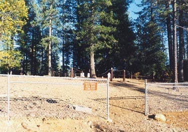 A fenced area with trees in the background and a sign that likely contains a warning or information.