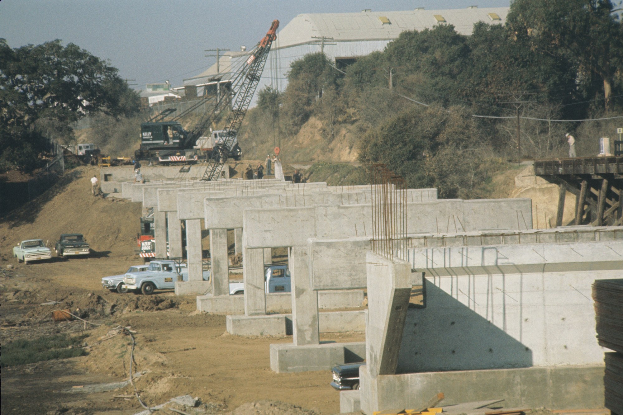 A construction site with concrete structures, a crane, workers, and vehicles.