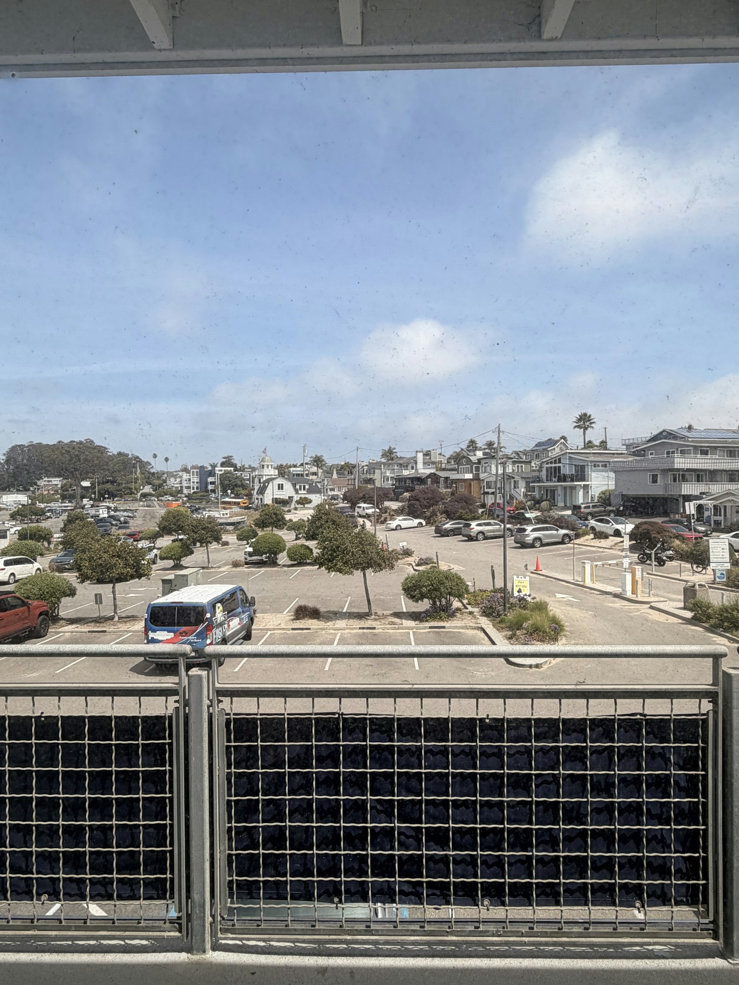 A view from a building showing a parking lot, cars, trees, and a clear sky with some clouds.