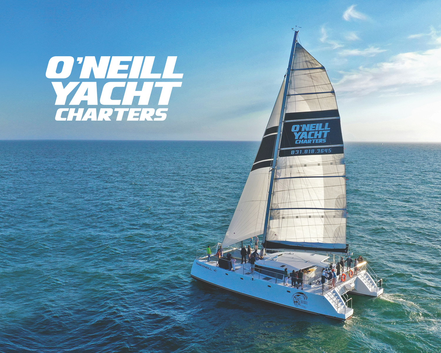 Sailing yacht on the ocean with passengers and "O'NEILL YACHT CHARTERS" branding on the sail.