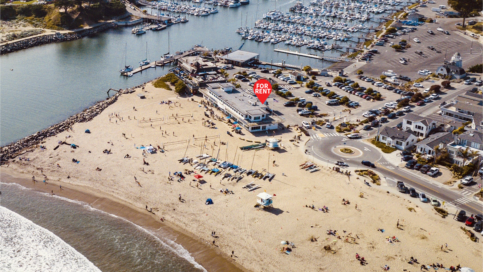 An aerial view of a beach area with a rental property, marina, and people enjoying the sand and water.