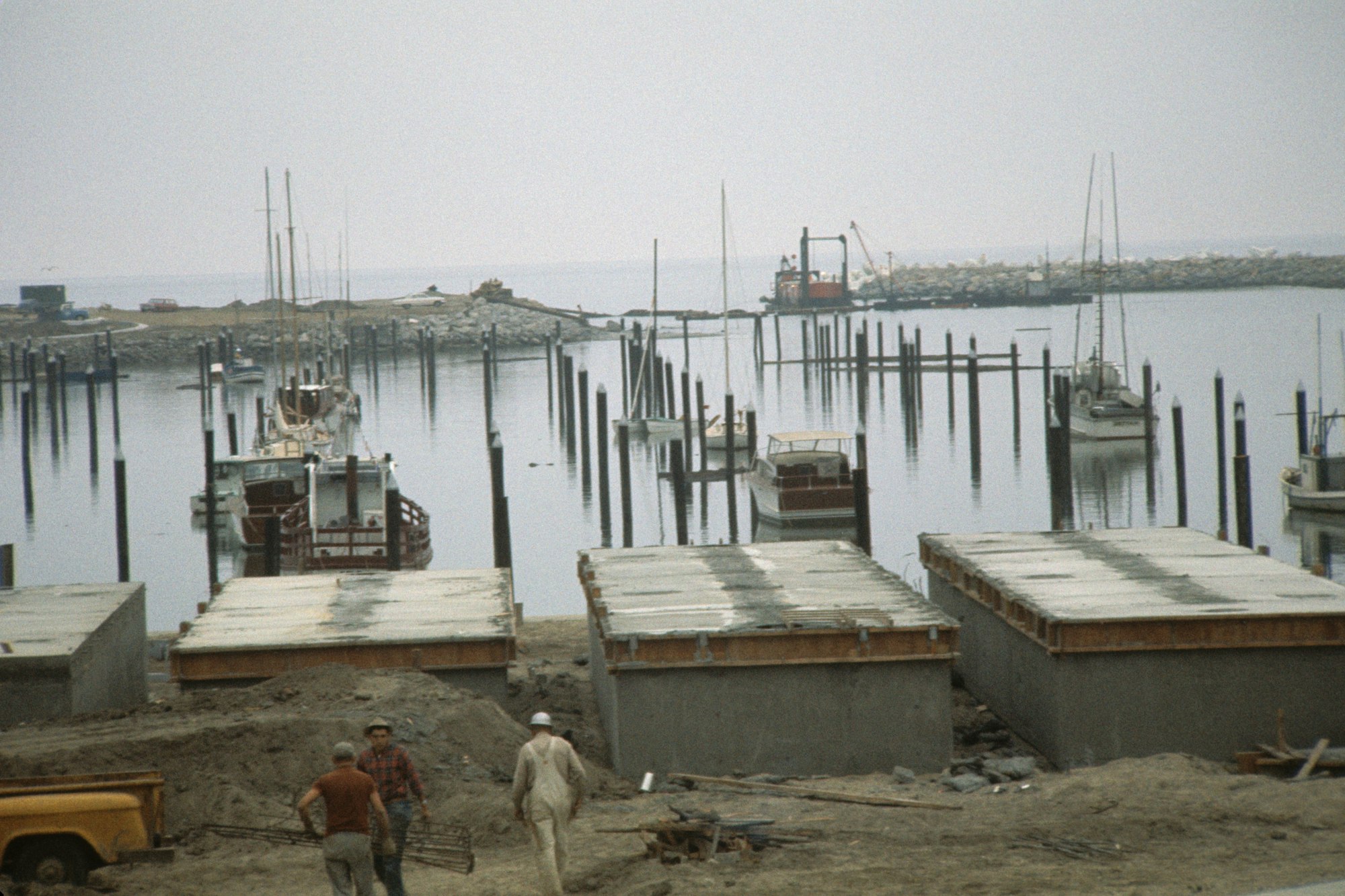 A harbor with boats, construction area, workers, and calm water.