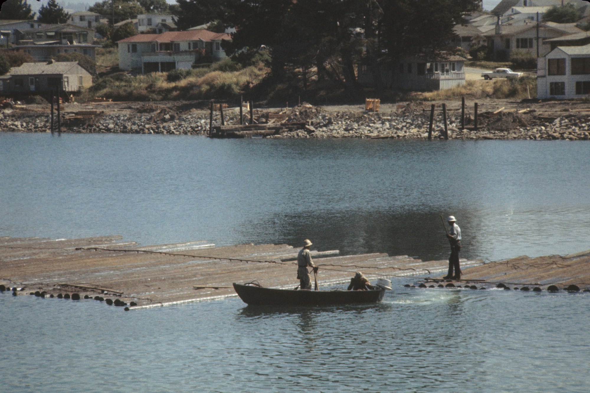 People on a boat and a jetty, with coastal houses in the background.