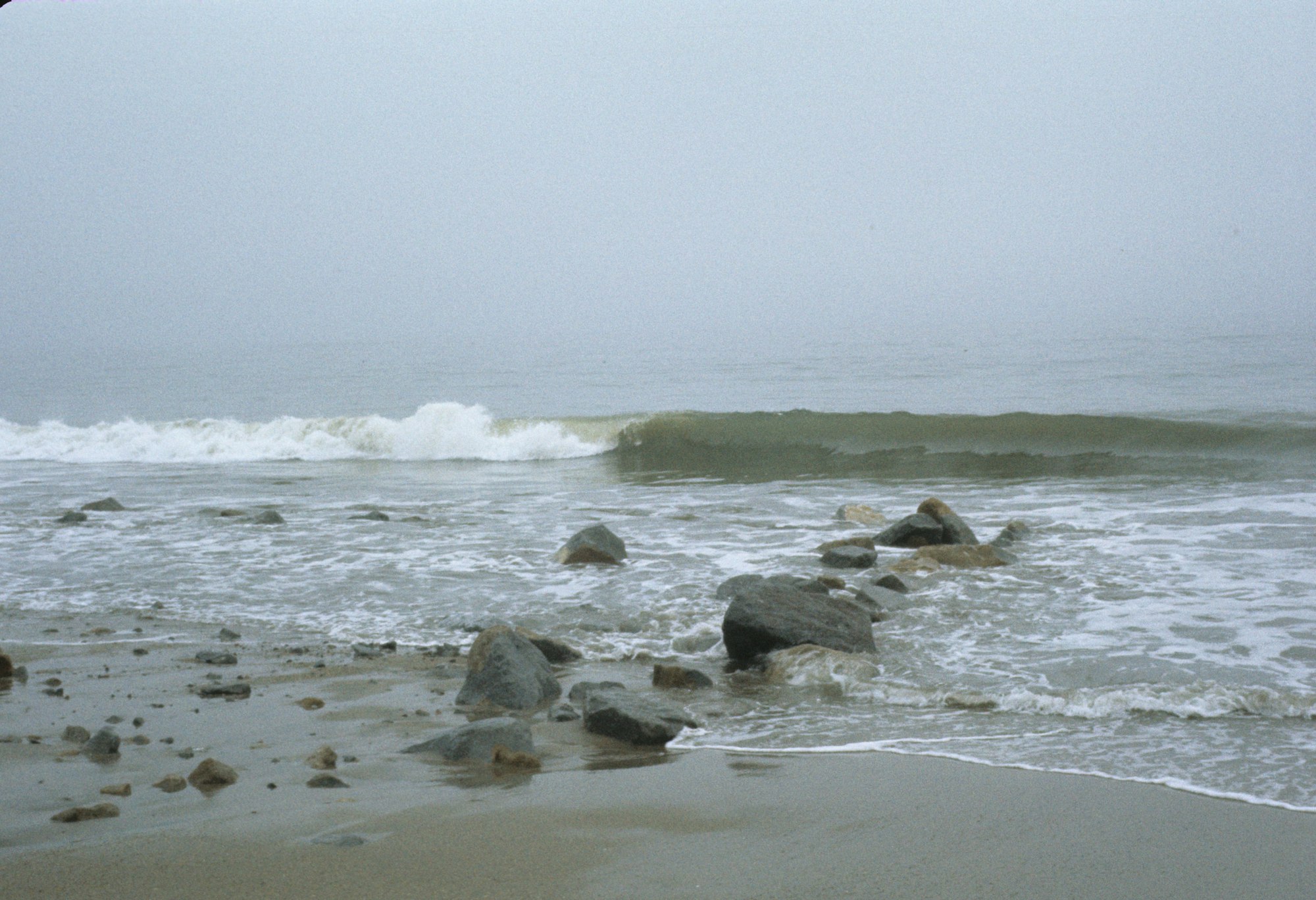Foggy beach with waves and scattered rocks.