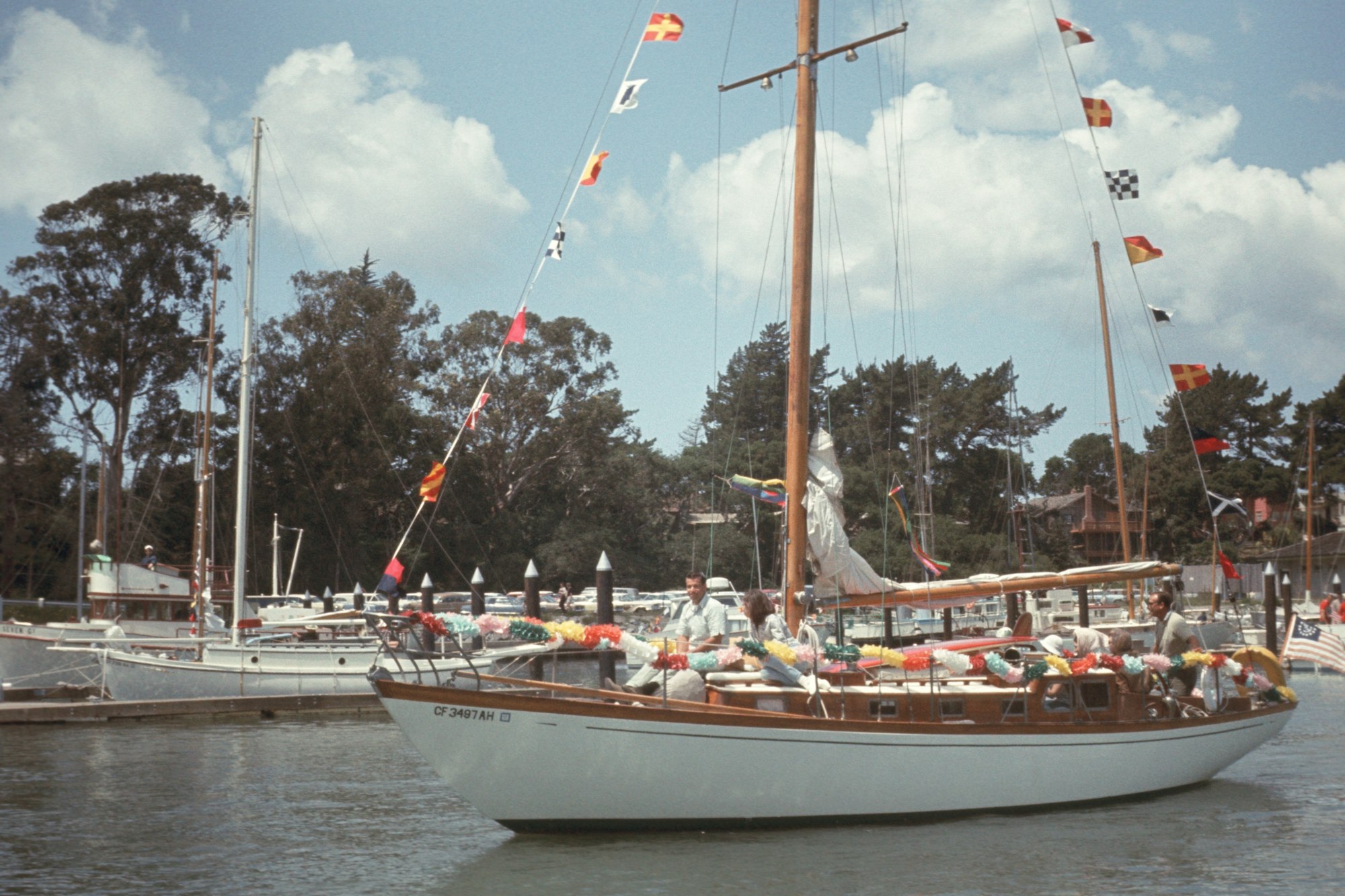 A sailboat adorned with colorful flags and passengers, docked in a marina under a blue sky.