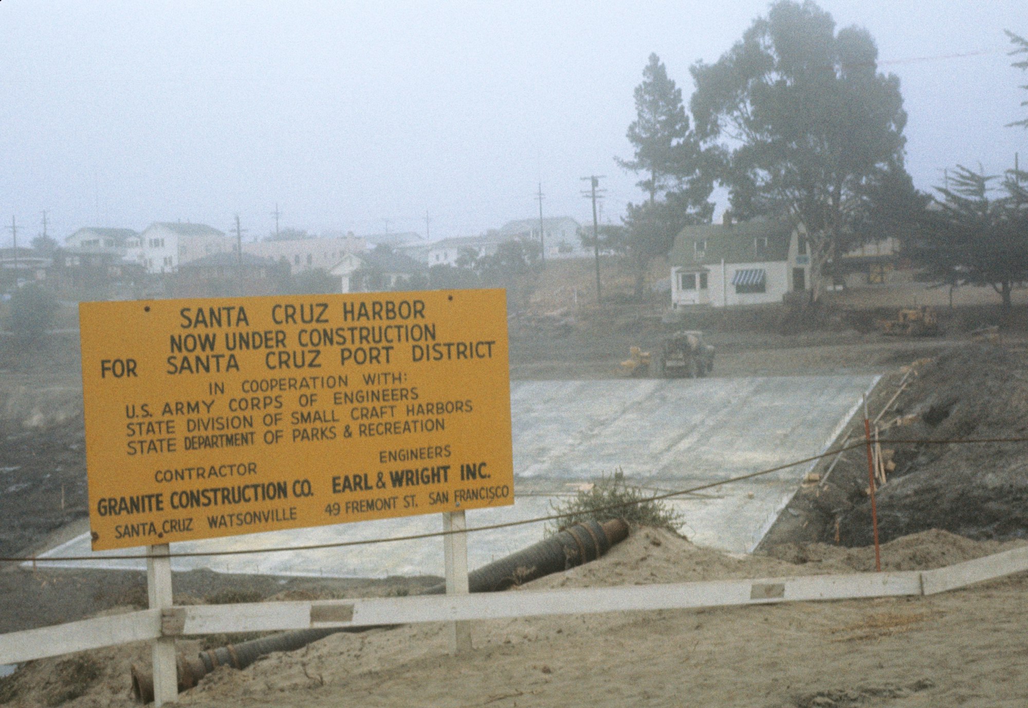 Construction site for Santa Cruz Harbor with informational sign, equipment and foggy backdrop.