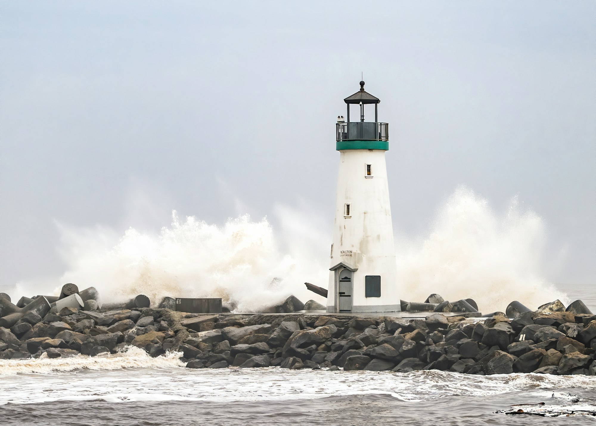 A lighthouse on a rocky shore with waves crashing against it.
