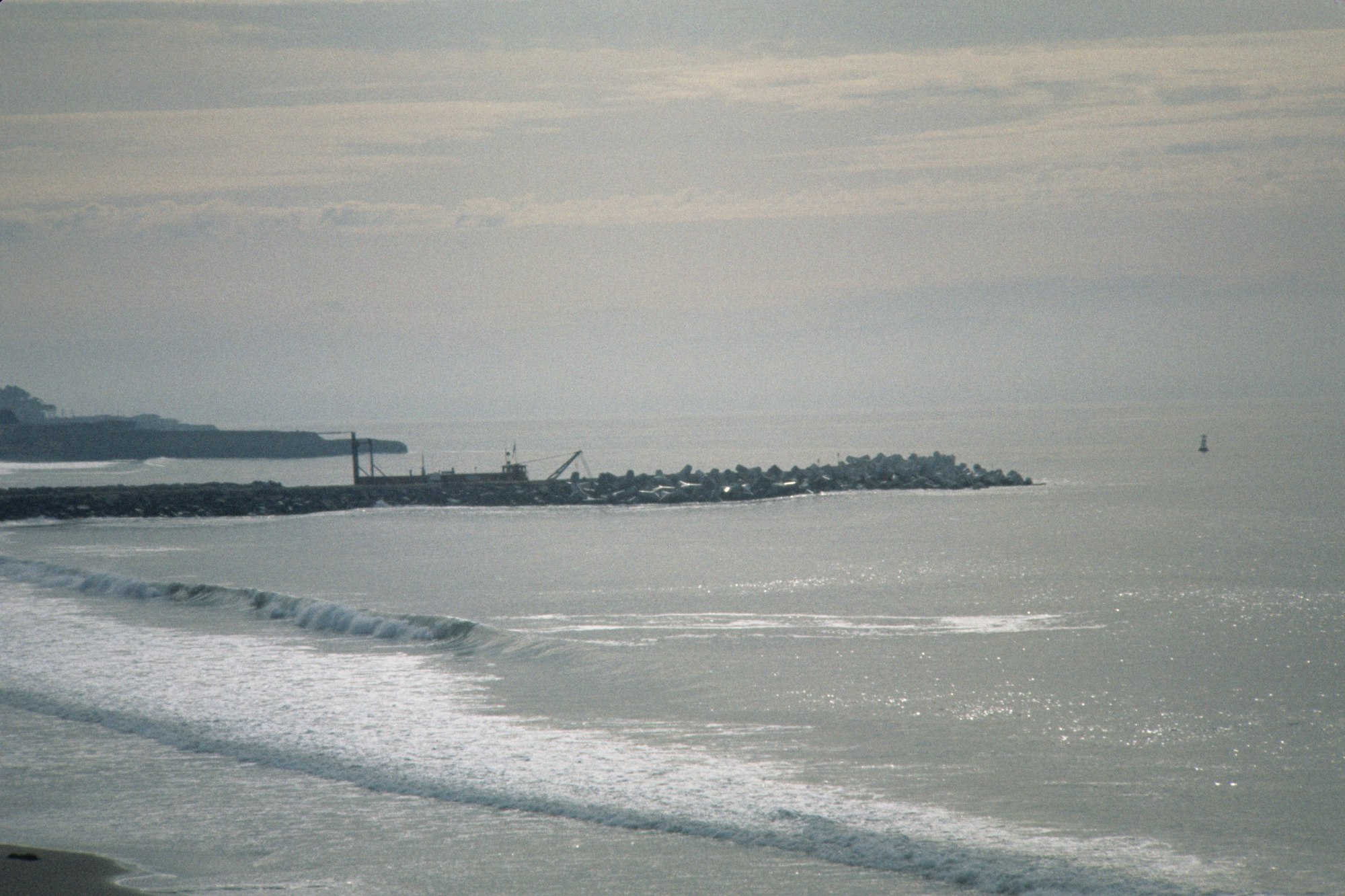 Coastal view with waves, breakwater, and hazy sky.