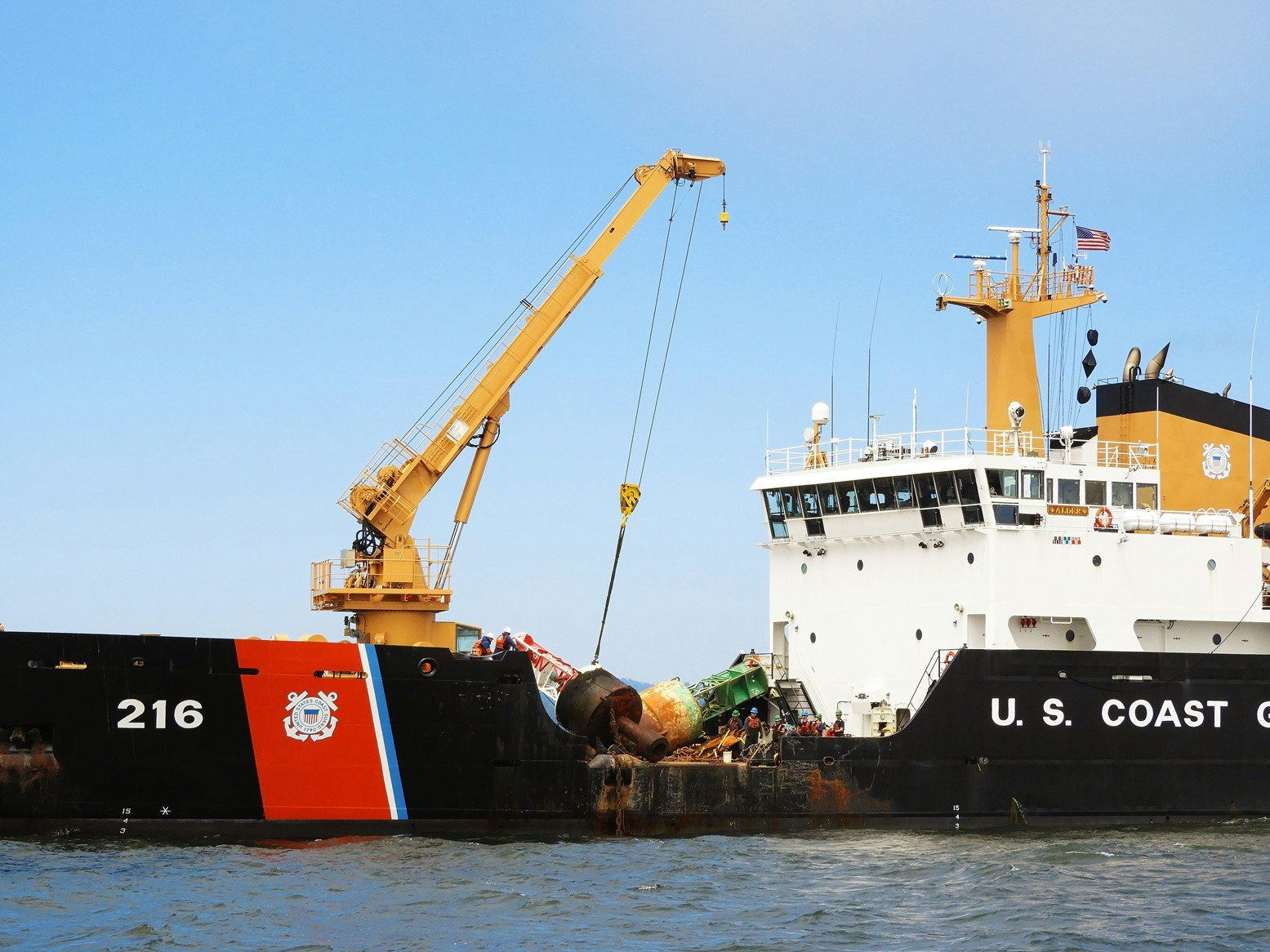 Coast Guard vessel with crane lifting debris, clear sky, calm sea.