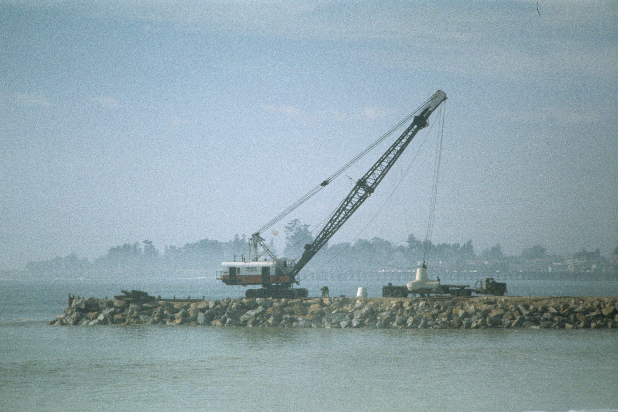 Crane on a rocky pier near water with foggy backdrop.