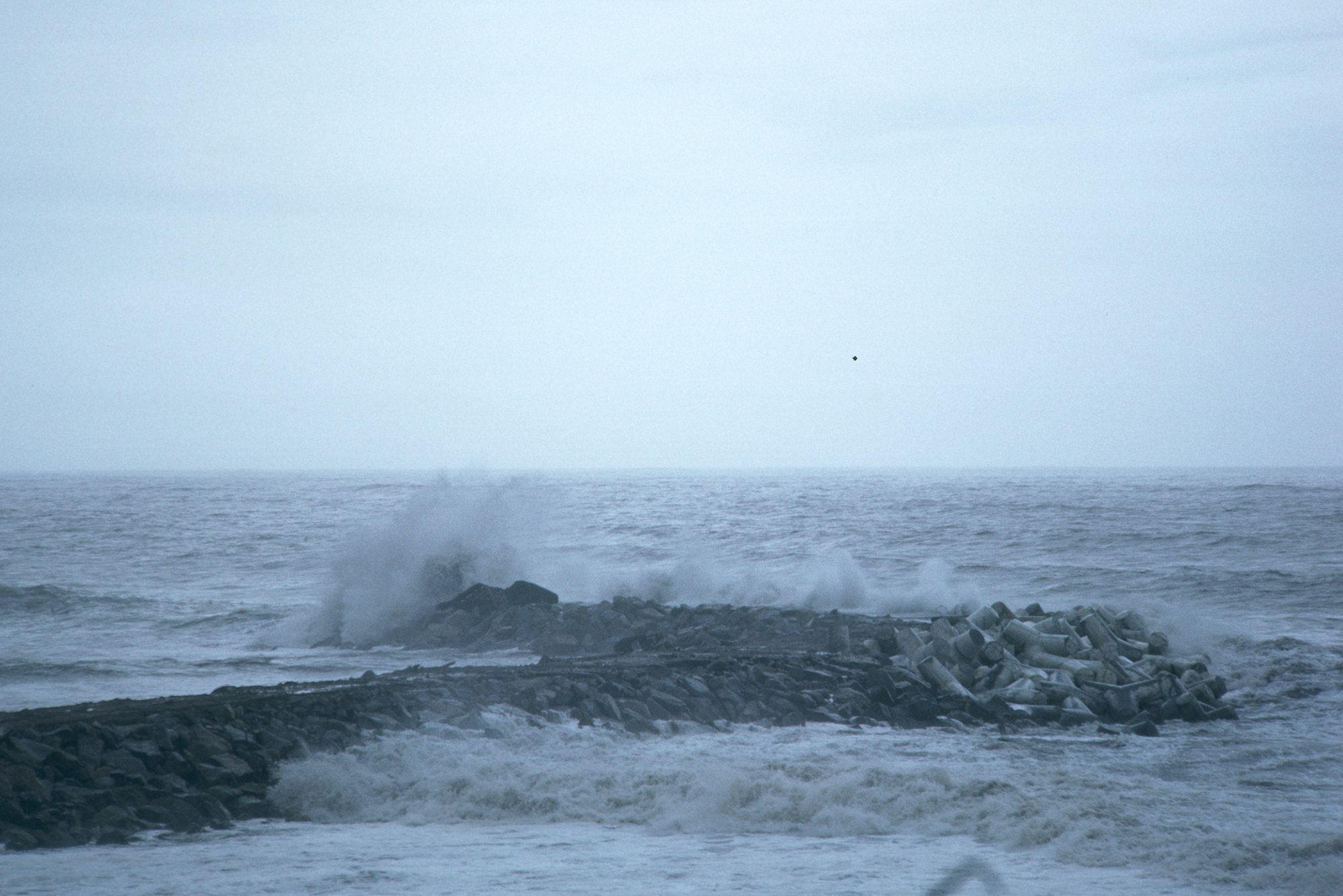Waves crashing against a rocky breakwater with a cloudy sky.