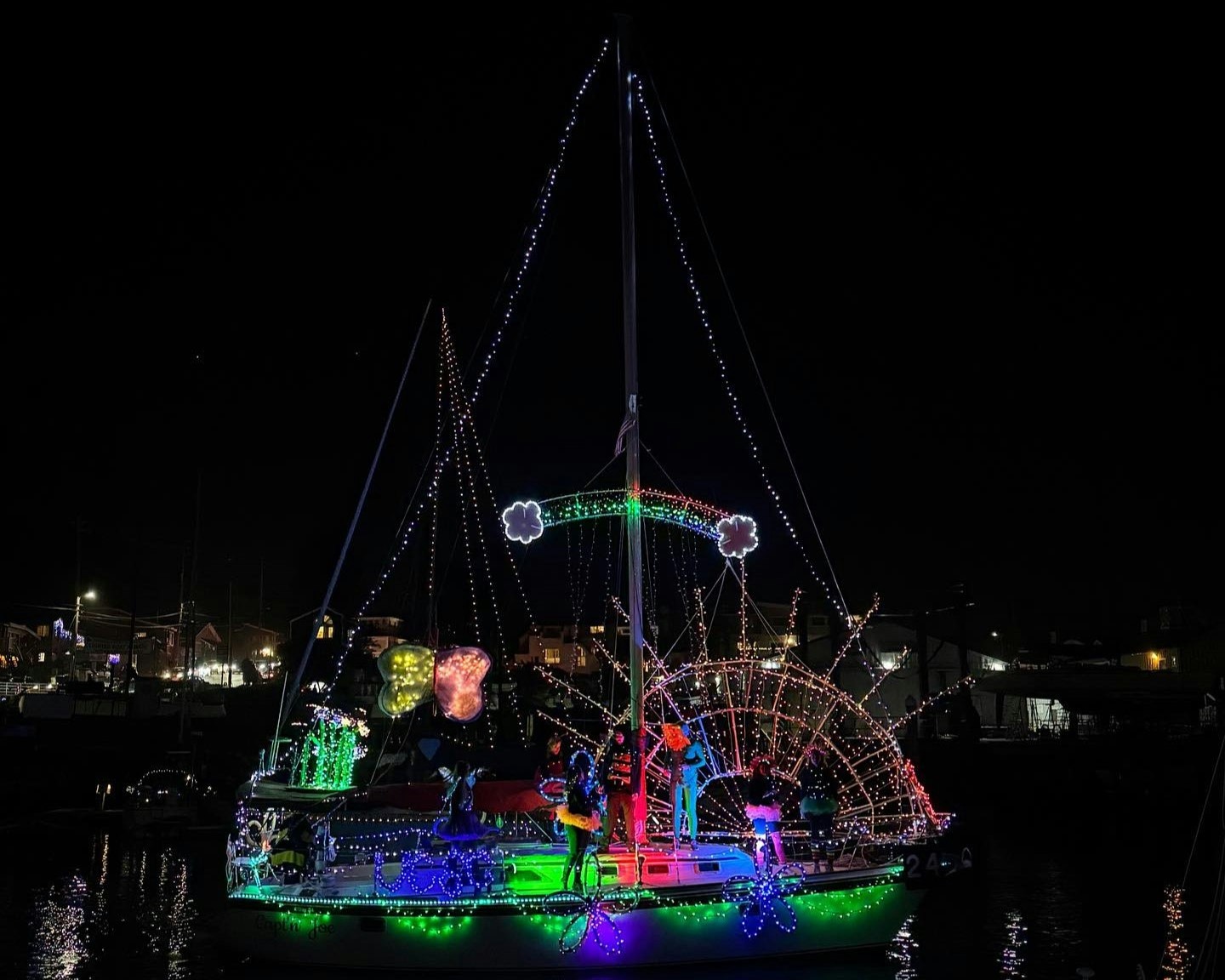 A boat decorated with colorful lights and whimsical figures, including a rainbow and flowers, against a dark night sky.