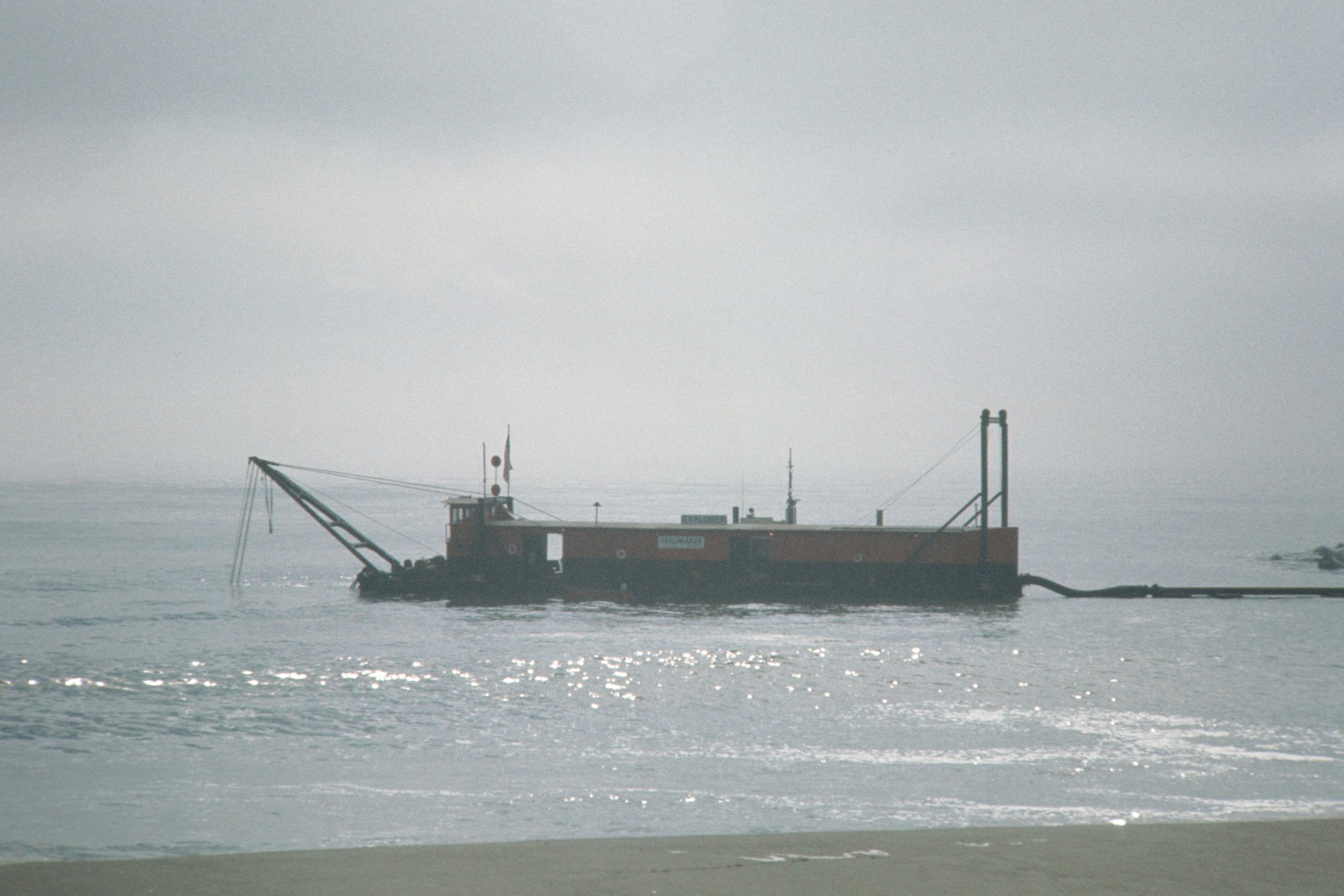 A barge with a crane on a misty beach.