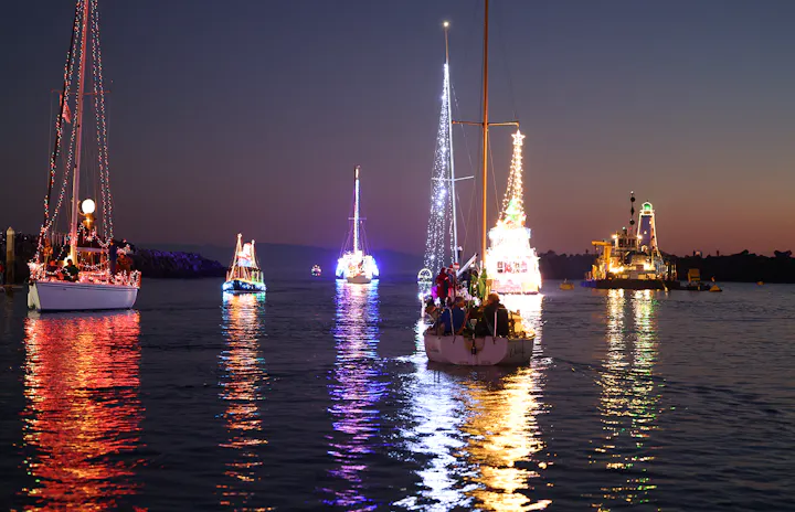A vibrant display of decorated boats illuminated at dusk, reflecting on the water during a festive celebration.
