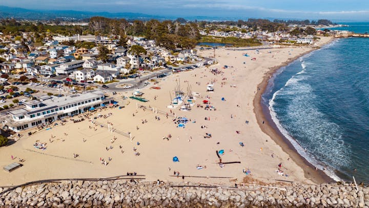 Aerial view of a coastal town with a sandy beach, boats, and people enjoying a sunny day.