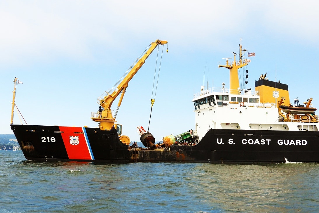 A U.S. Coast Guard ship with a crane lifting equipment from the water.