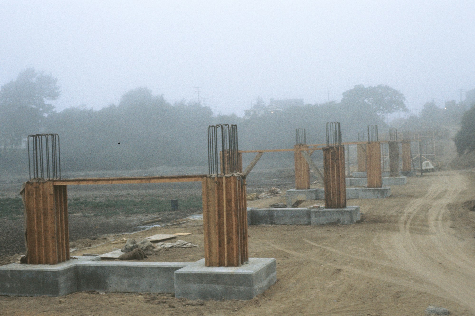 A foggy construction site with unfinished concrete pillars and steel reinforcements.